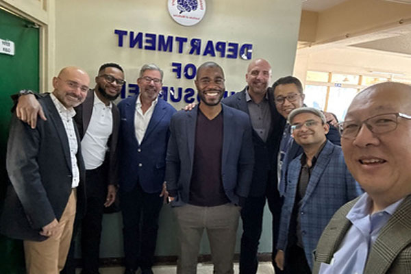 A group of men in professional attire smiling for a photo in front of a Department of Neurosurgery sign.