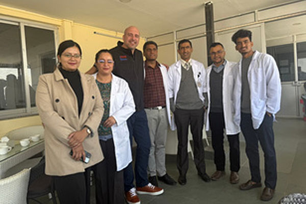 A group of medical staff in white coats and professional dress posing for a photo on a balcony or porch.
