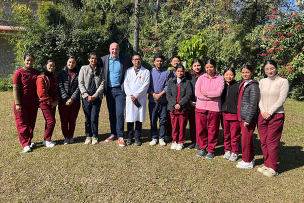 A group of students in red scrubs and medical staff standing together outside near green trees.