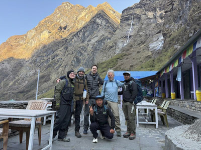 Group of hikers posing together outside a mountain lodge with towering rocky peaks behind them.
