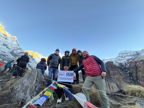Group of trekkers holding a banner in front of a majestic, sunlit mountain range.