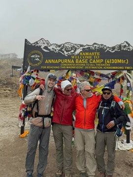 Four men posing under a sign that reads "Namaste Welcome to Annapurna Base Camp (4130Mtr.)".
