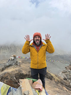 Hiker in a yellow jacket making a funny face on a foggy mountain peak.