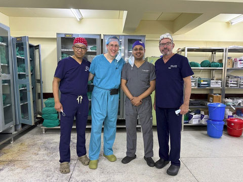 Four surgeons posing in medical scrubs inside an operating room storage area.