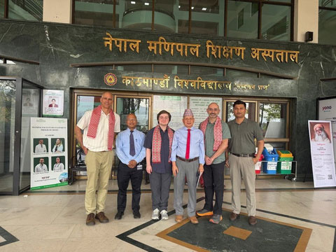 Six men standing outside the Nepal Manipal Teaching Hospital entrance.
