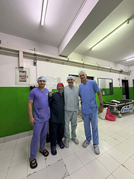 Four medical professionals in scrubs posing inside a green-walled hospital room.