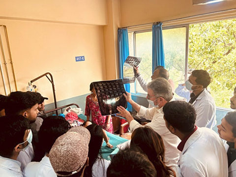 Medical professionals and students gathered around a hospital bed, reviewing large spinal MRI films with a senior clinician.