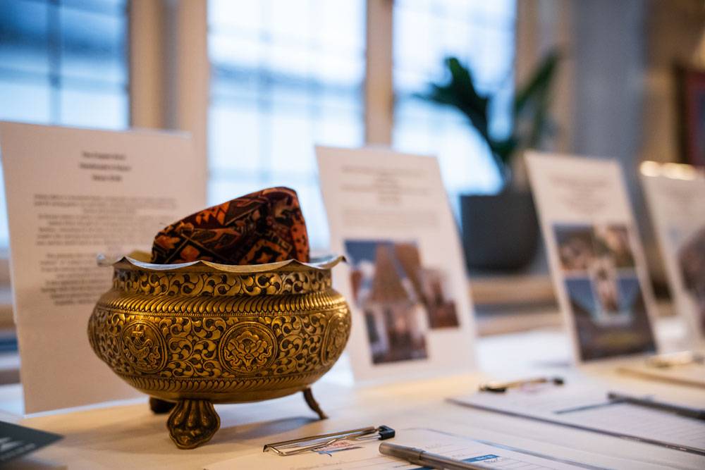 An ornate, footed brass bowl sits on a table in front of informational event flyers.