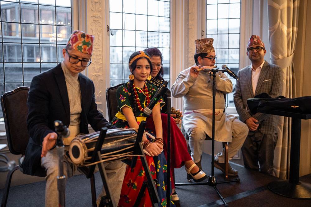 Musical performers on a stage including a man playing a traditional drum and another playing a flute.