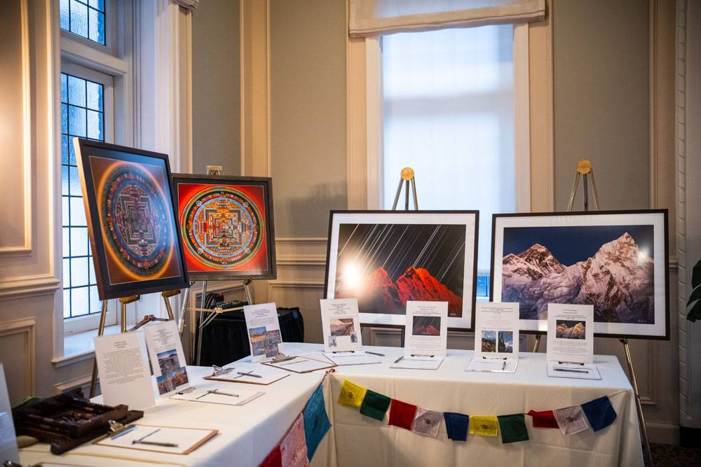 Silent auction table featuring framed mountain photography, colorful mandalas, and prayer flags.